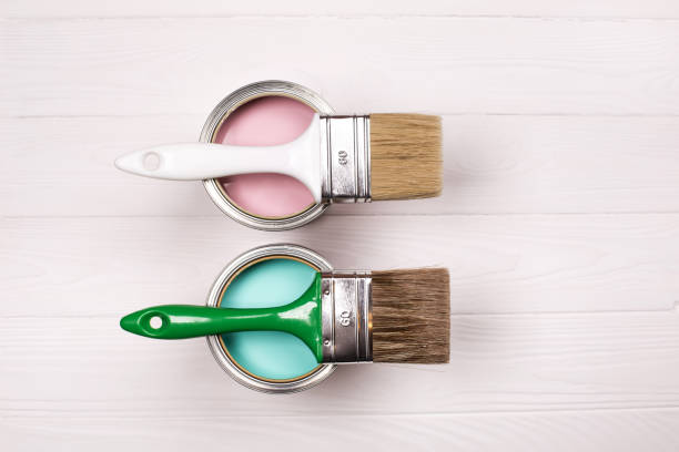 Two pink and blue open paint cans and brush on white wooden background.