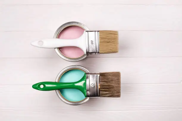 Two pink and blue open paint cans and brush on white wooden background. House renovation concept.