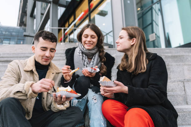 tre giovani viaggiatori con salsiccia al curry all'aperto a berlino - currywurst foto e immagini stock