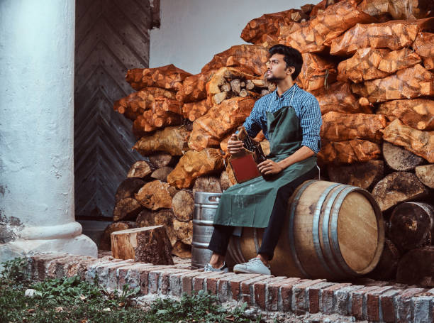 fatigué de brasseur au tablier assis sur une bière artisanale baril et boissons détente après le travail. - after work beautiful people beer beer bottle photos et images de collection