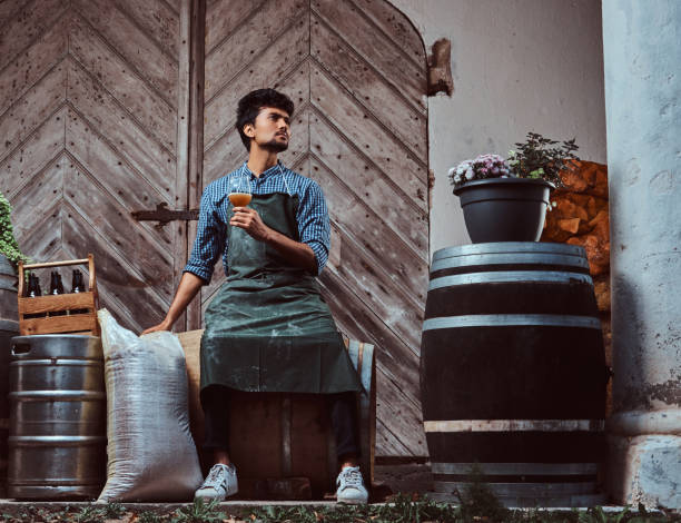 maître brasseur, assis sur le tonneau en bois et titulaire d’un verre de bière artisanale se détend après le travail. - after work beautiful people beer beer bottle photos et images de collection