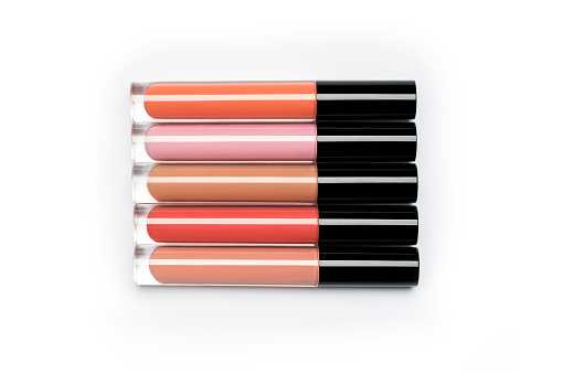 Five brightly coloured bottles of liquid lipstick and lip gloss arranged in a row on clean white background shot with studio light from above