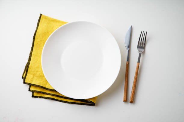 istock White empty plate with knife and fork and yellow textile napkin on white background 1070737980