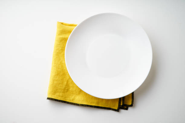 istock White empty plate with yellow textile napkin on white background 1070738332