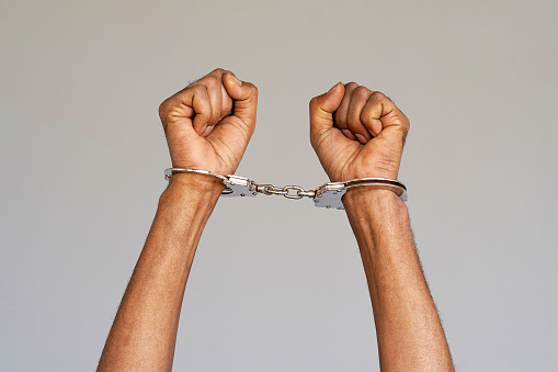 Close-up. Arrested african man handcuffed hands. Prisoner or arrested terrorist, close-up of hands in handcuffs. Isolated on gray background