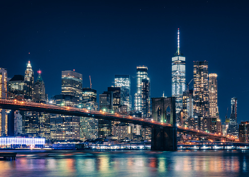 A long exposure of New York City Brooklyn Bridge at night featuring skyscrapers, stars in the Sky and the World Trade Centre and the East River