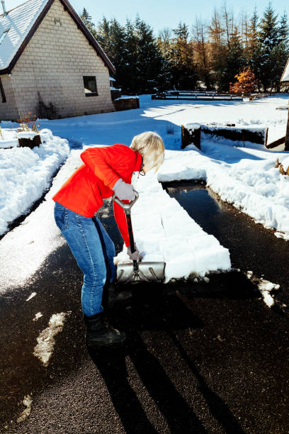 Senior woman clearing snow from her front yard using a wide snow shovel.