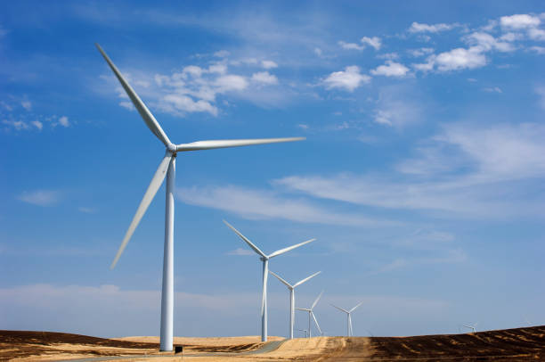 Wind Turbines lined up along a coastal wind turbine farm, with clouds in background.
