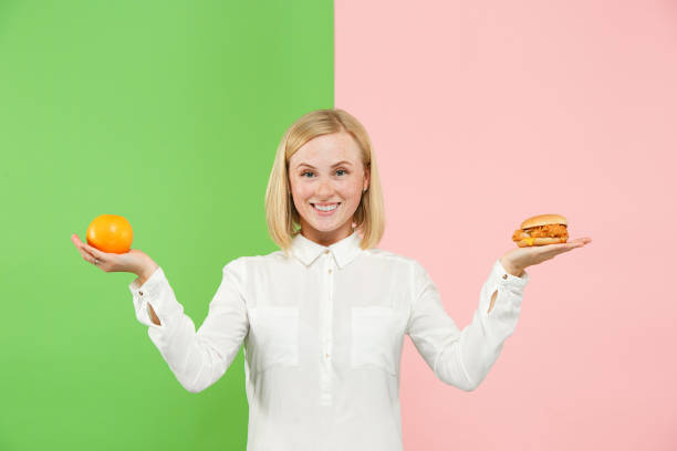 dieta. concepto de dieta. alimentos saludables. hermosa mujer joven elegir entre frutas y comida rápida de unhelathy - comparison apple orange isolated fotografías e imágenes de stock