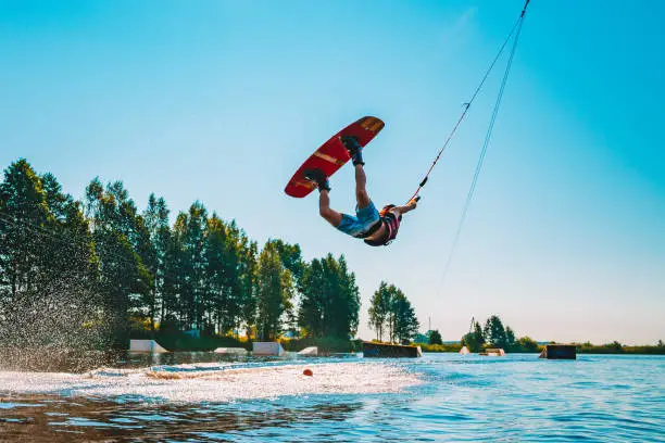 Marupe, Latvia. July 20, 2018. Young man wakeboarding on a lake, making raley, frontroll and jumping the kickers and sliders. Wakeboard.