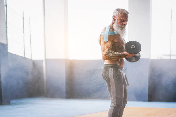 istock Fitness beard man doing biceps curl exercise  inside a gym - Tattoo senior man training with dumbbells in wellness club center - Body building and sport fit concept 1070773264