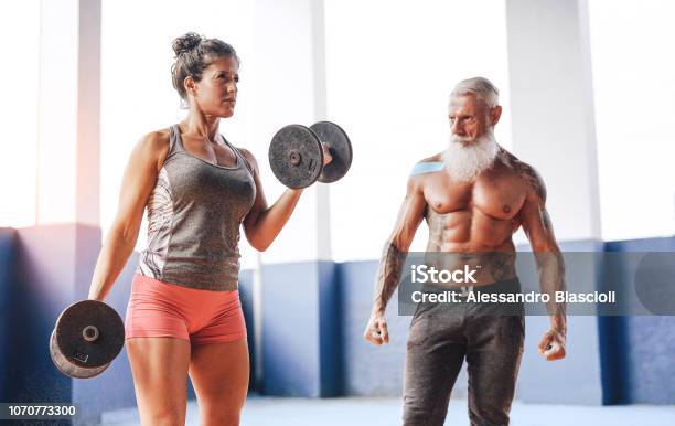 Photo libre de droit de Femme Fit Faire De Lexercice Biceps Curl Avec Haltères Dans Un Centre De Fitness Gym Athlète Féminine De Formation Avec Son Entraîneur Personnel À Lintérieur Wellness Sport Club Entraînement Et Le Concept De Motivation Sportive banque d'images et plus d'images libres de droit de Troisième âge