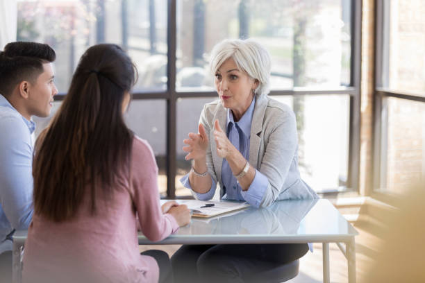 Serious counselor advices young couple Serious Caucasian senior female counselor gestures while giving important advice to a young married couple. marriage counseling stock pictures, royalty-free photos & images