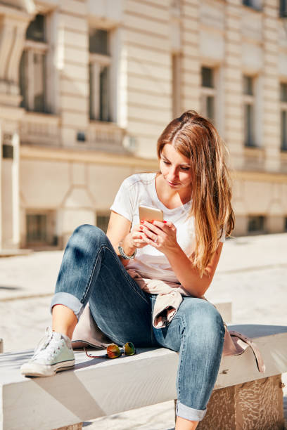 istock Young attractive woman using cellphone while sitting on the bench outdoors. 1070777092