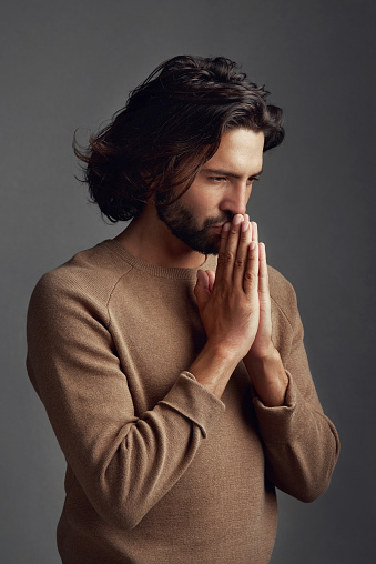 Studio shot of a handsome young man praying against a gray background