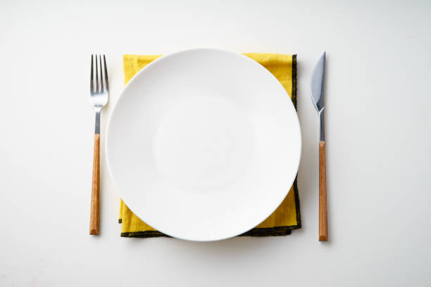 istock White empty plate with knife and fork and yellow textile napkin on white background 1070787236