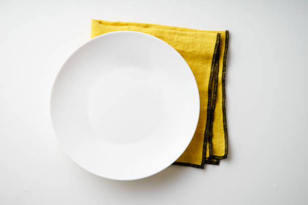 istock White empty plate with yellow textile napkin on white background 1070787240