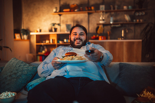 Hombre con sobrepeso comer comida rápida y viendo televisión photo