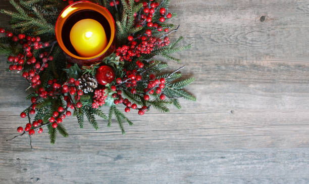 Christmas Candle with Evergreen Tree Branches and Berries Over Rustic Wood
