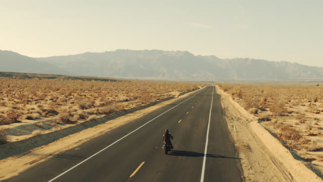 Aerial view of man riding motorcycle down desert road at sunset