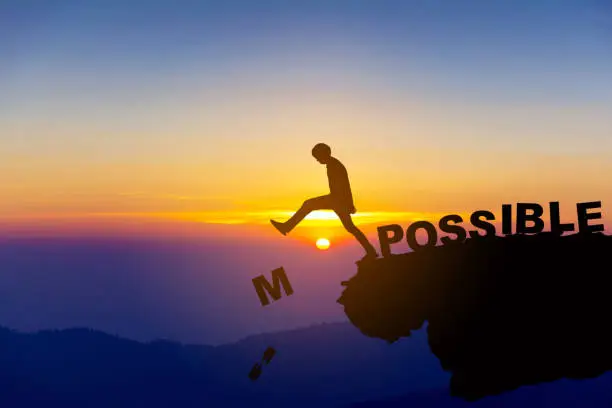 Photo of Silhouette man pushing letters I and M from the rock. Word 'possible' standing sound. Sunrise sky at background. Concept of opportunity,copy space.
