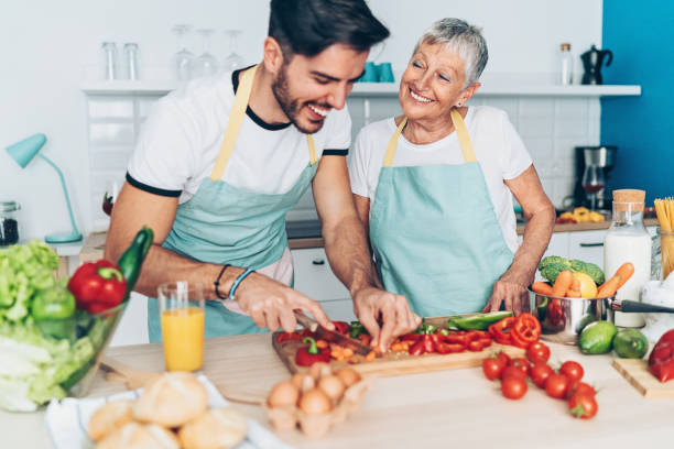 madre e figlio adulto che fanno insalata insieme - grandmother senior adult family domestic kitchen foto e immagini stock