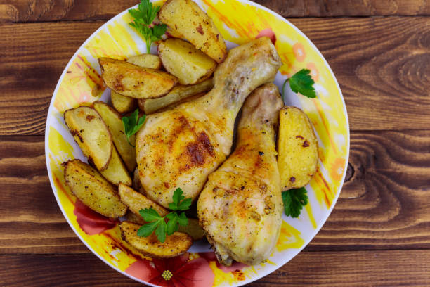istock Baked chicken drumsticks with potatoes in a plate on wooden table 1070850620