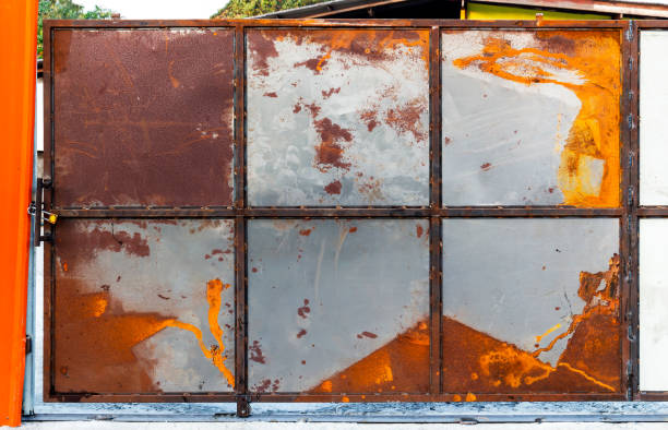 istock Gate is made of ld rusted galvanized metal sheet with old locked padlock. Rusty surface caused by oxidation iron with orange and brown cracked color for design work texture and background. 1070861224