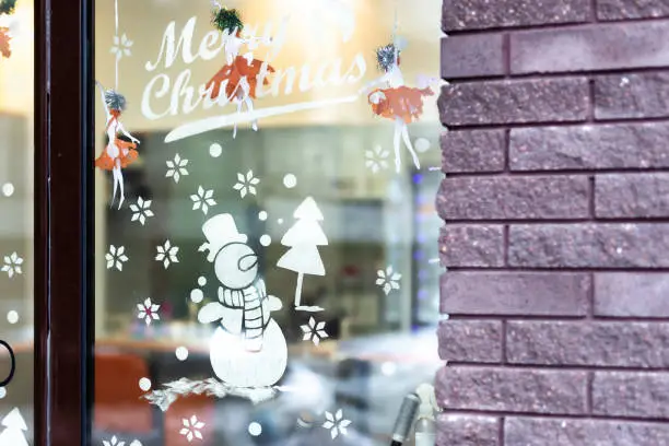 Shop-window decorated with temporary drawing of snowman and christmas tree made of artificial snow. New year and xmas holidays city decor.