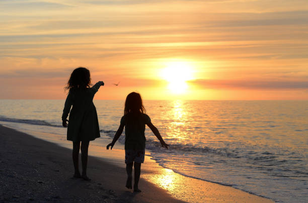 A breathtaking beautiful sunset over the ocean on the West Coast of Florida. Two children in silhouette run, play, and enjoy freedom, frolic and childhood. tranquil ocean and idyllic pastel horizon, nature at it's finest and we feel the joy and exuberance of kids at play in an idyllic setting