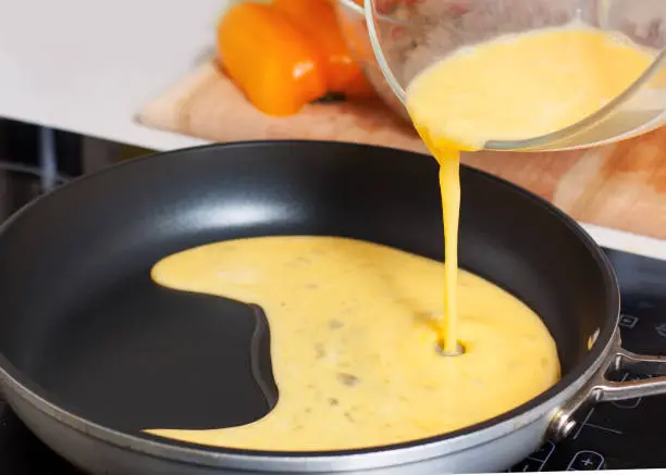 Preparation of Mexican chicken omelet. Pouring beaten eggs on hot frying pan with oil
