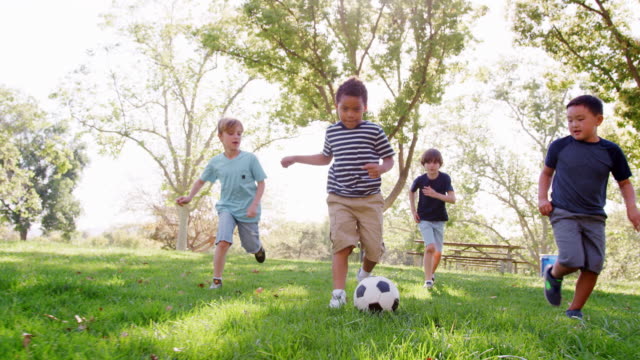 Group Of Young Boys With Friends Playing Football In Park Shot In Slow Motion