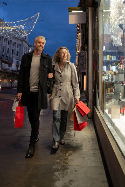 Happy couple Christmas shopping in London Happy couple Christmas shopping in London and looking at a shop window while carrying shopping bags - lifestyle concepts window shopping at night stock pictures, royalty-free photos & images