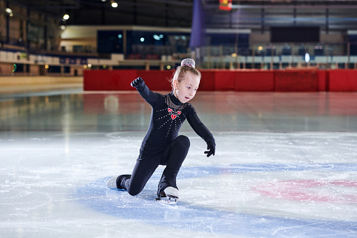 Full length portrait of little girl figure skating in indoor rink during competition or training, copy space