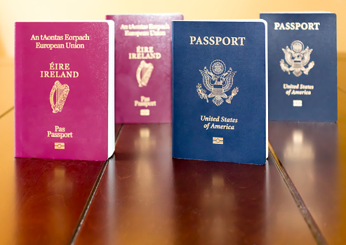 Irish (European Union) and United States of America Passports standing next to each other, and reflected on a wooden table.