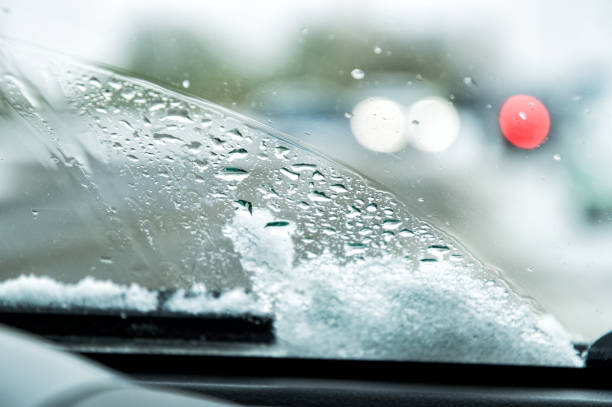 istock Snow-covered car windshield with melted snow drops and windshield wipers. Blurred lights of passing cars and the city street on the background. Copy space. 1070908116