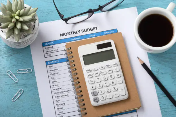Photo of Monthly budget with white calculator on blue table