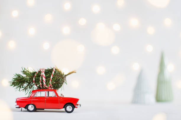 Red toy car with a christmas tree on the roof, garland bokeh on background stock photo