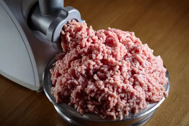 Minced meat coming out from modern electric grinder on oak table. Healthy fresh homemade minced meat. Place for copyspace.