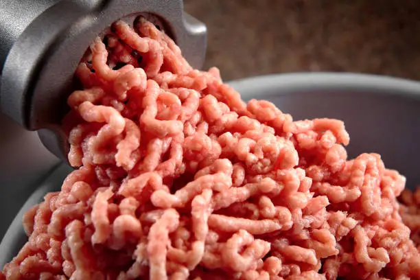 Minced meat coming out from modern electric grinder close-up. Healthy fresh homemade minced meat. Place for copyspace.
