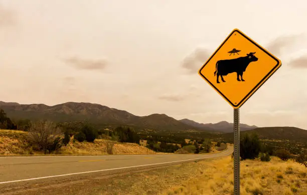 Photo of Cow Alien Abduction Road Sign along the Turqoise Trail, Route 66 Scenic Byway, in springtime between Santa Fe and Albuquerque, New Mexico.
