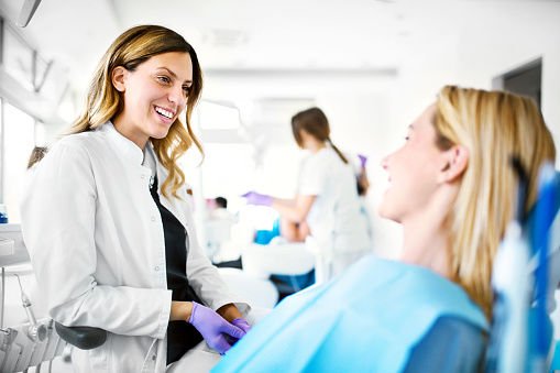 Young cheerful female dentist listening issues that female patient having with her teeth.
