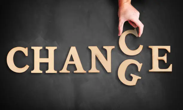 hand is moving a wooden letter, turning the word "change" to "chance" on a blackboard