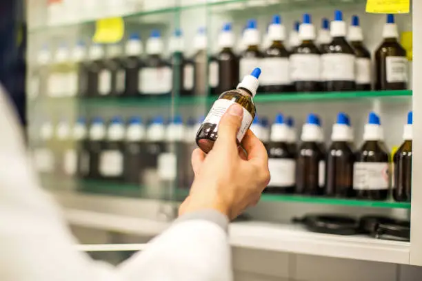 Close up of male pharmacist hand looking at medicine bottle from the self in pharmacy. Pharmacist holding a medicine bottle in hand.