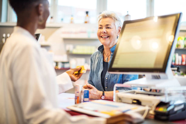 Chemist giving the card to costumer after the payment Female pharmacist returning the credit card to female client after receiving the payment. Chemist giving the card to costumer after the payment. chemist stock pictures, royalty-free photos & images