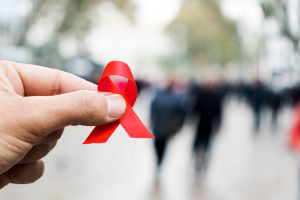 man with a red ribbon for the fight against AIDS closeup of a red awareness ribbon for the fight against AIDS in the hand of a young caucasian man in a busy pedestrian street of a city aids stock pictures, royalty-free photos & images