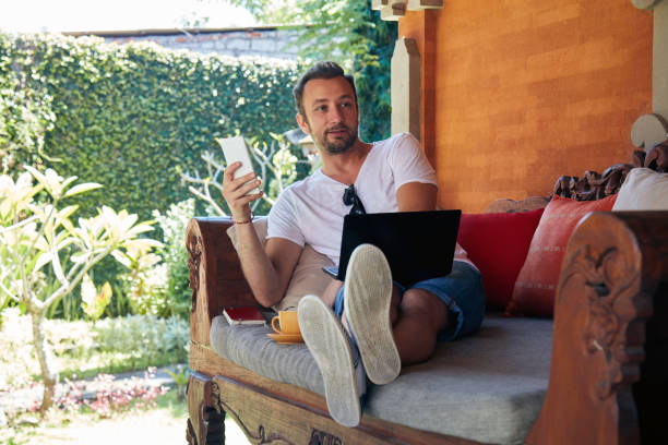 istock Man using cellphone and laptop while drinking coffee / tea on the porch. 1070962888