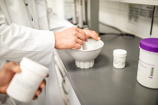 Hands of male scientist preparing medicine in pharmacy lab. Man mixing medicine in bowl.