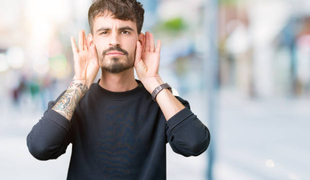 istock Young handsome man over isolated background Trying to hear both hands on ear gesture, curious for gossip. Hearing problem, deaf 1070964634