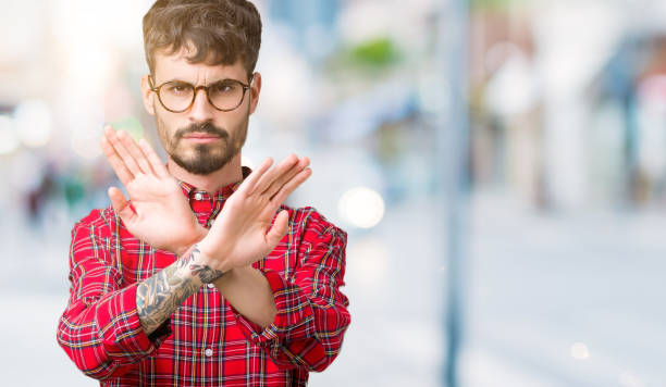 istock Young handsome man wearing glasses over isolated background Rejection expression crossing arms and palms doing negative sign, angry face 1070964736